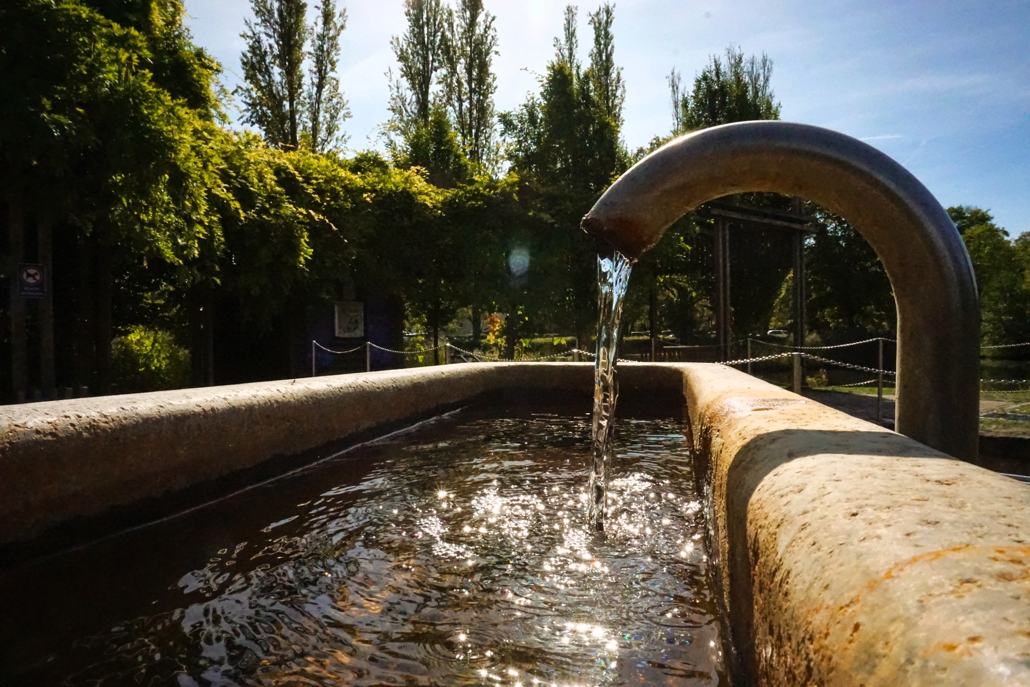 Kneipp-Becken auf der Kneipp-Insel im Kurpark Bad Windsheim, Nahaufnahme Wasser läuft ins Becken im Gegenlicht der Sommersonne