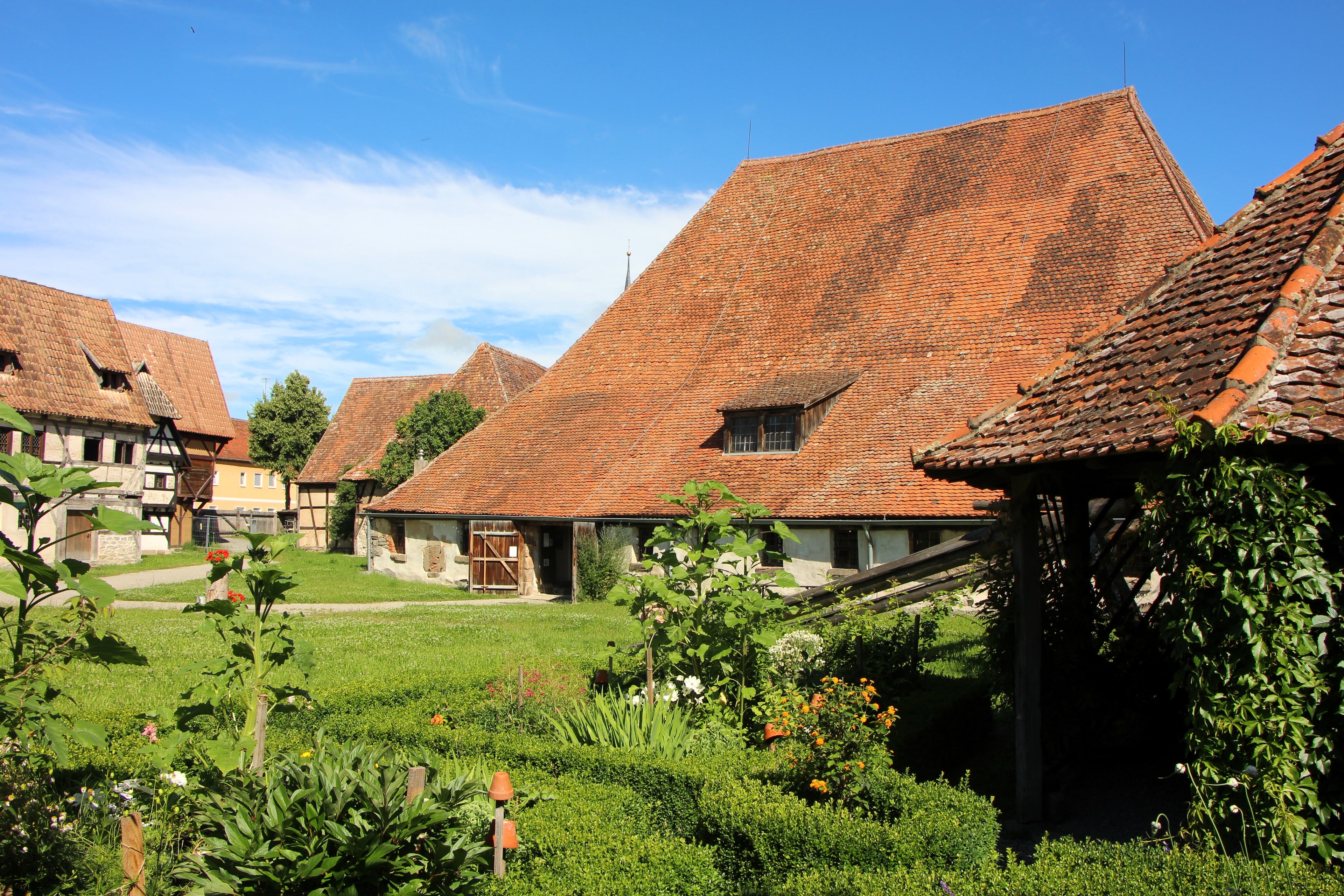 Der Alte Bauhof von Bad Windsheim mit seinem einmaligen, imposanten, historischen Dachstuhl von der rückwärtigen Seite fotografiert, im Vordergrund ein blühender Kräutergarten