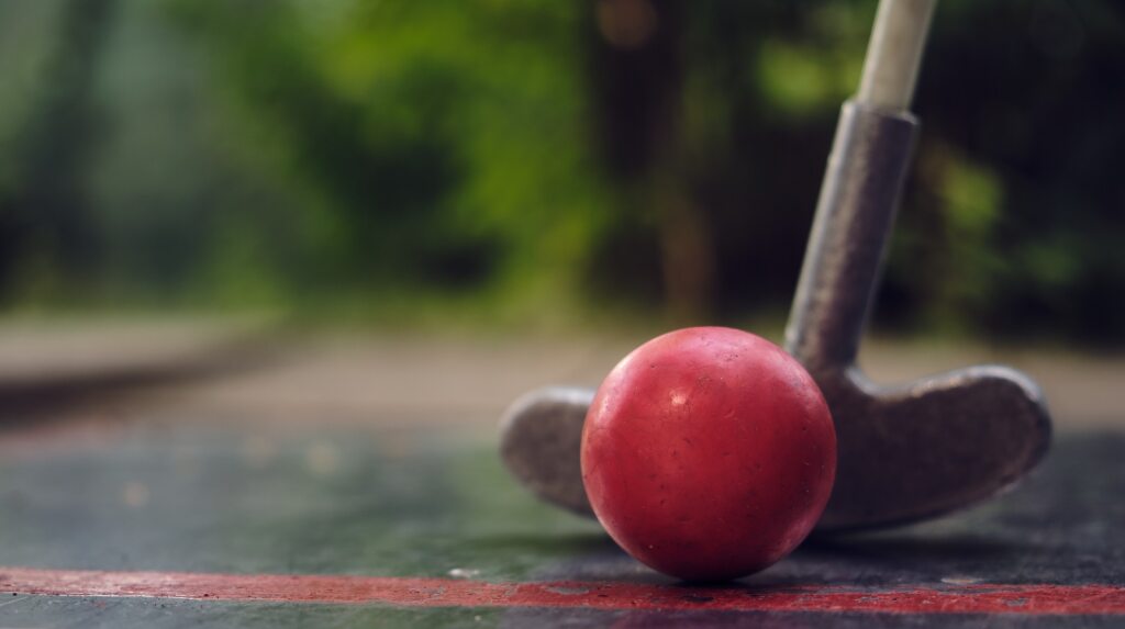 Roter Minigolfball im Vordergrund dahinter der Schläger