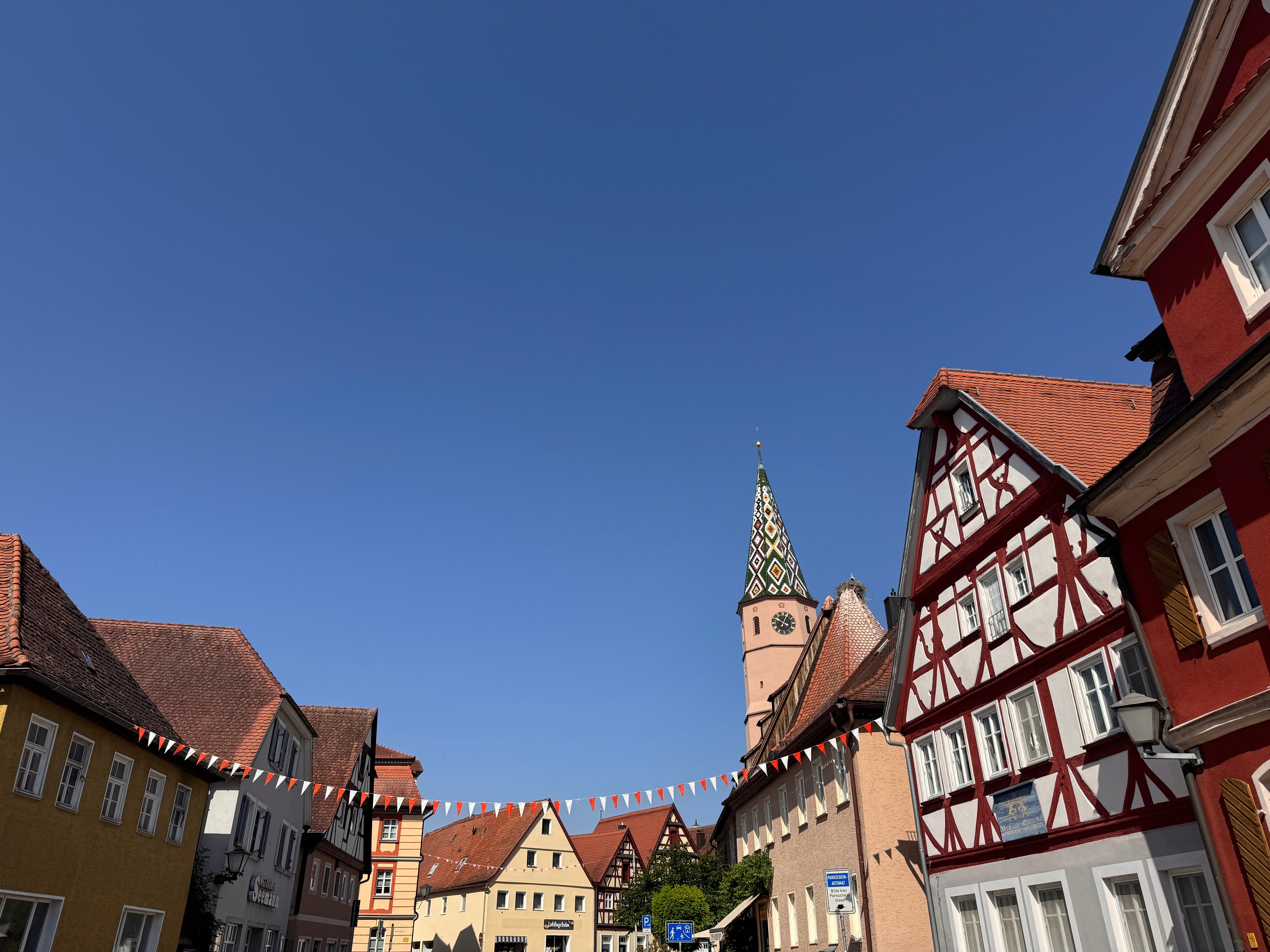 Seegasse in Bad Windsheim, historische Gebäude, die Seekapelle mit ihrem bunten Kirchturm, Störche auf dem Dach des Kirchenschiffs, Wimpel in rot-weiß schmücken die historische Altstadt von Bad Windsheim, die Kulisse vor strahlend blauem Sommerhimmel ohne ein Wölkchen, das anerkannte Heilbad zeigt sich von seiner schönsten Seite