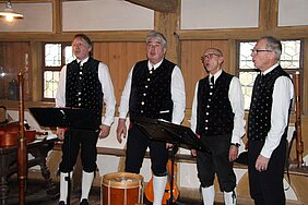 Vier Männer in Tracht stehen in einer Reihe und singen