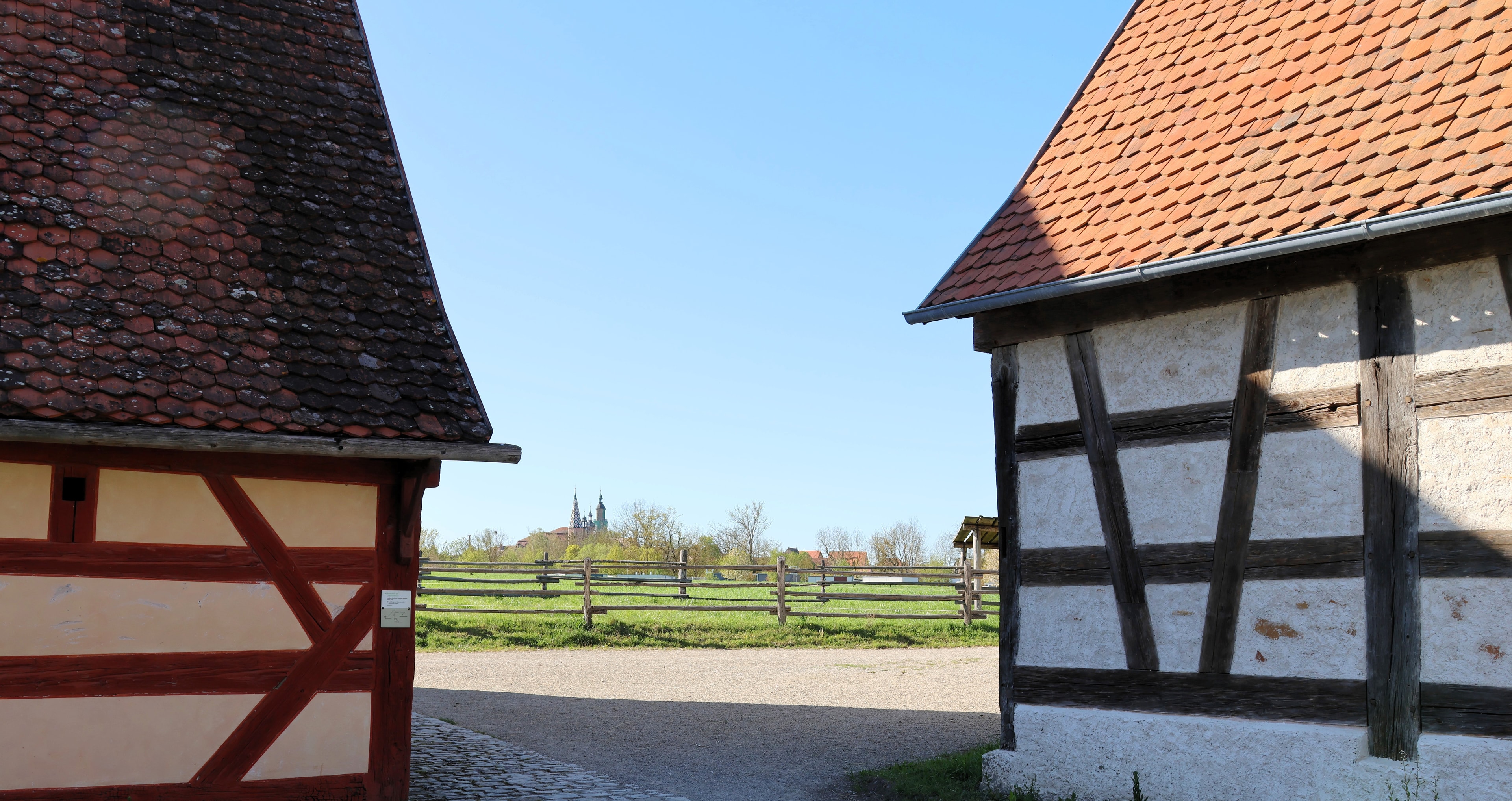 Zwei Fachwerkhäuser des Fränkischen Freilandmuseums in Bad Windsheim am linken und rechten Bildrand im Anschnitt. Im Hintergrund ist vor blauem Himmel die Stadtkulisse des mittelfränkischen Heilbads zu erkennen.