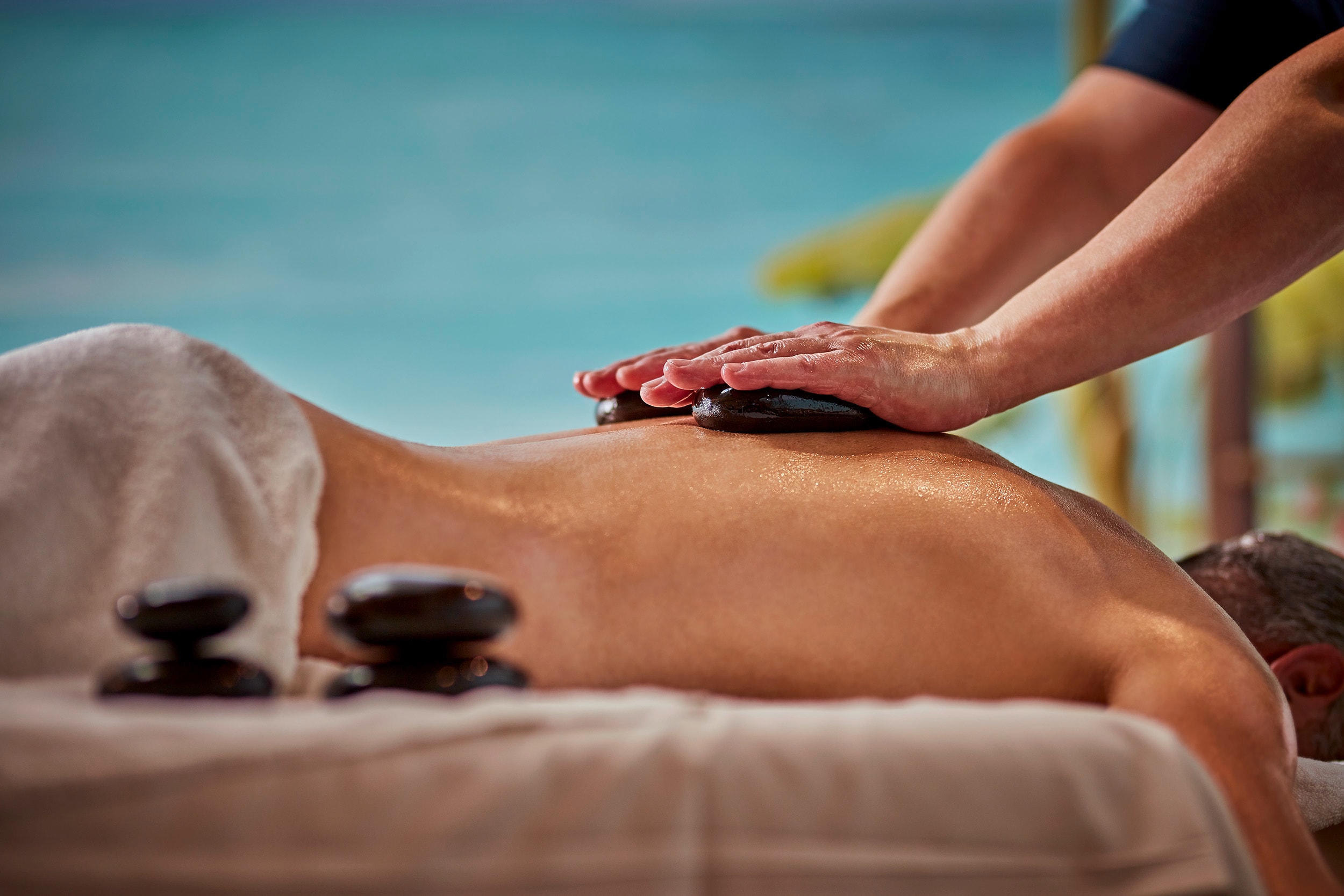 Eine Person wird von einem Mann am Rücken mit heißen Steinen massiert