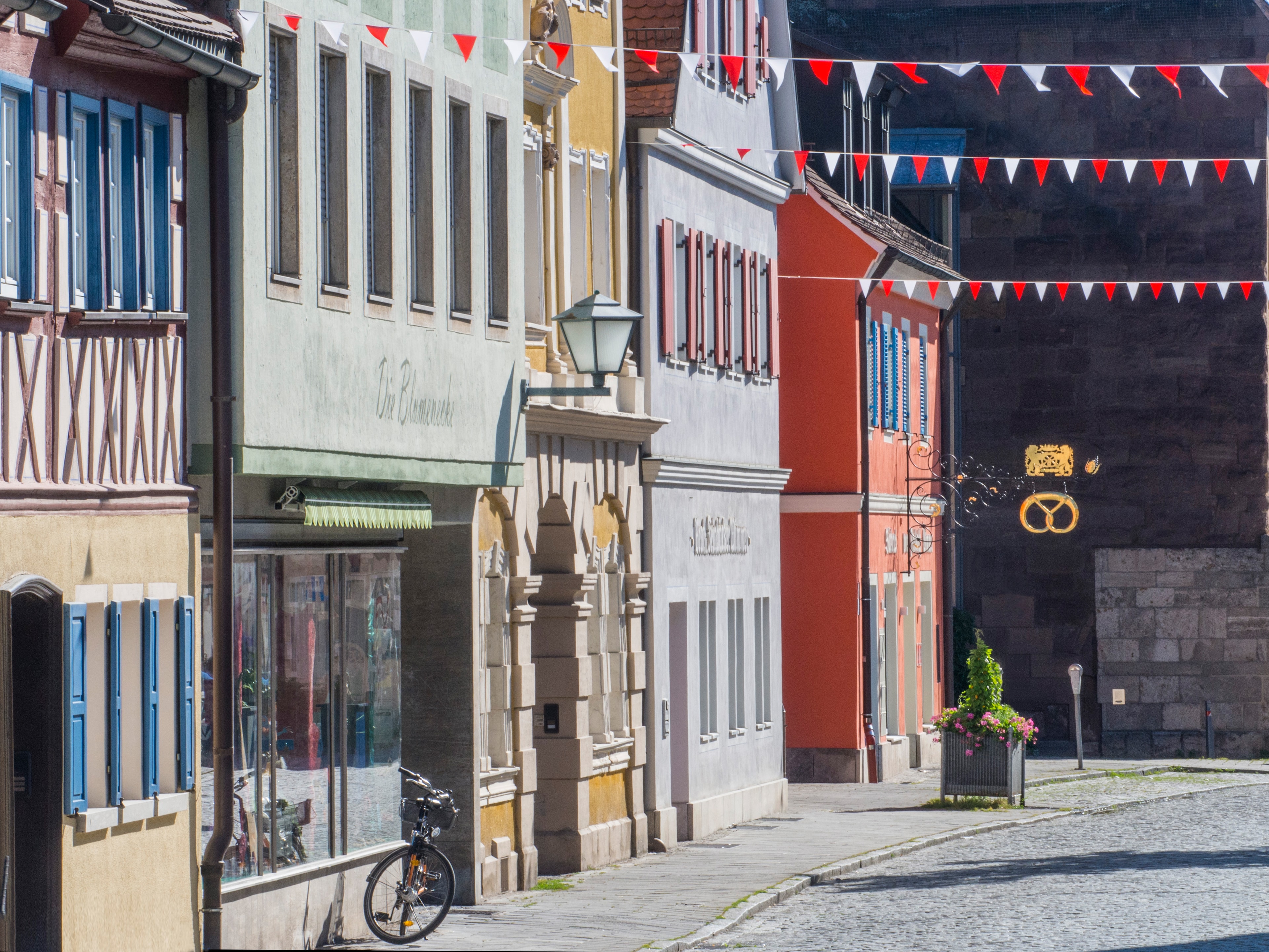 Blick in eine Gasse der historischen Altstadt von Bad Windsheim, Kopsteinpflaster, ein goldene Breze markiert eine Backstube, über der Straße sind weiß-rote Wimpel gespannt, der Frankenrechen